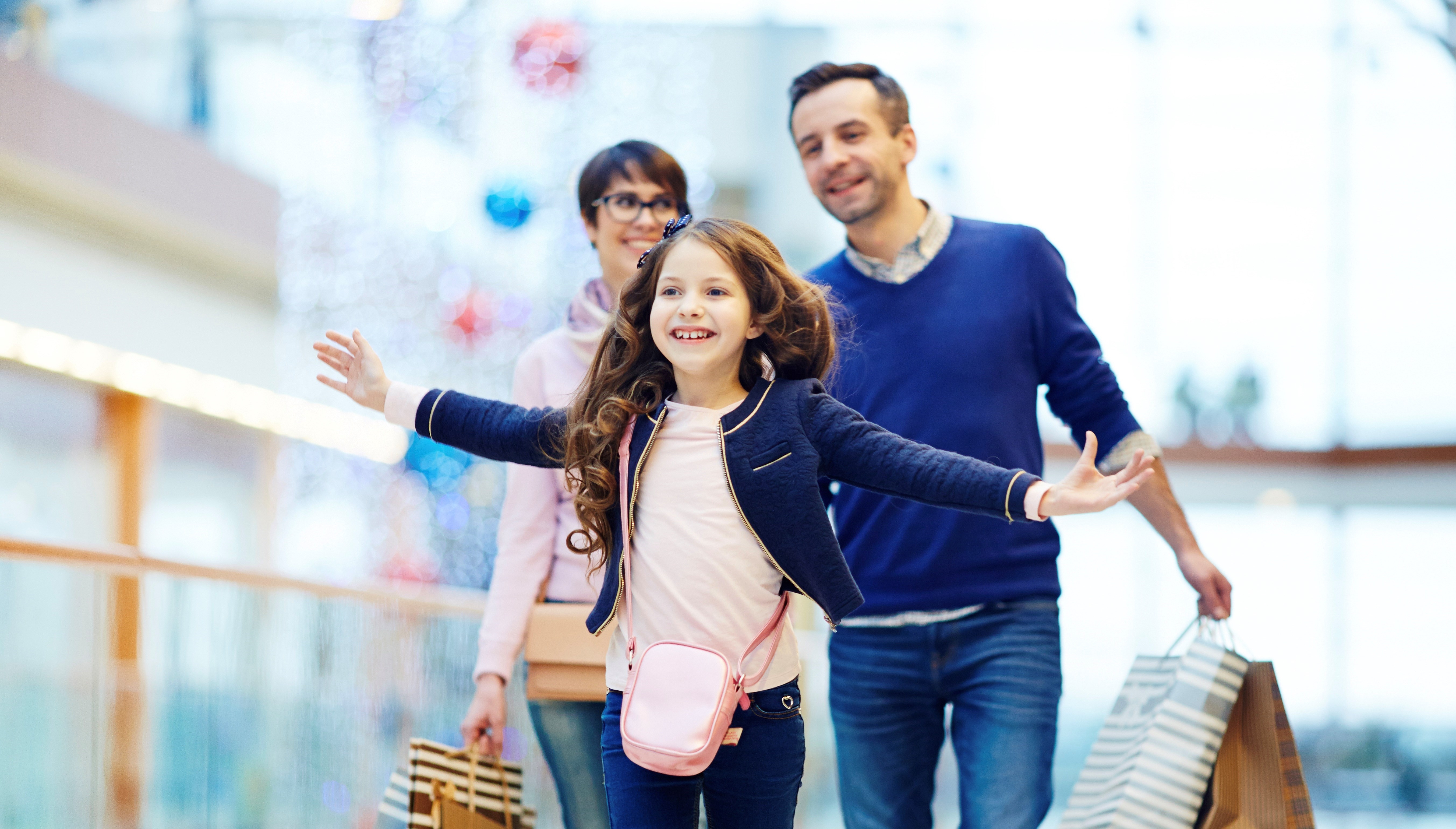 Joyful girl and her parents enjoying weekend in the mall